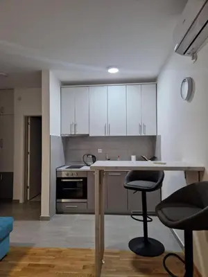 a kitchen with white cabinets and a table and two stools at Stan na Dan 39- PLAVI in Banja Luka