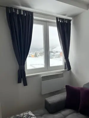 a living room with a window with blue curtains at Apartman Zimski Kutak in Kupres