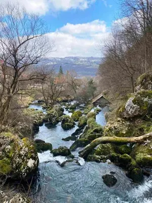 a river with rocks and a house in the background at Apartman Slapovi in Banja Luka