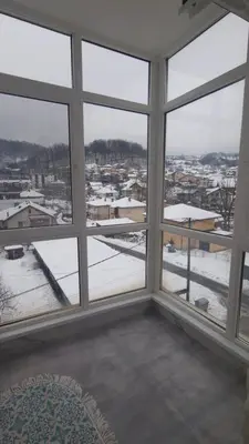 a room with large windows looking out at a snowy city at Stan na dan Čaršija in Gračanica