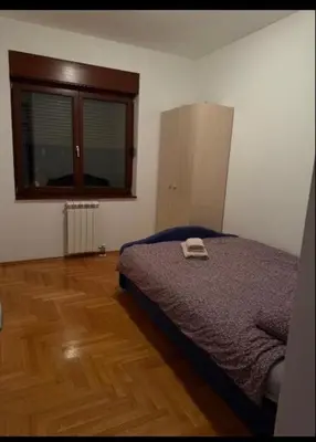 a bedroom with a bed and a window and a wooden floor at Trojka in Banja Luka