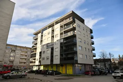 a tall building with cars parked in a parking lot at Apartman Nika in Banja Luka