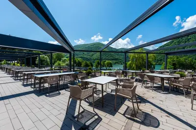 a patio with tables and chairs with mountains in the background at Hotel Plivsko jezero in Jajce