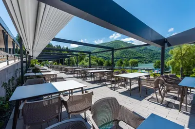 a patio with tables and chairs with mountains in the background at Hotel Plivsko jezero in Jajce