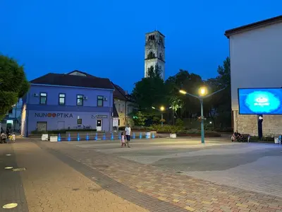 a person walking down a street at night with a clock tower at Apartments & Rooms Fountain in Bihać