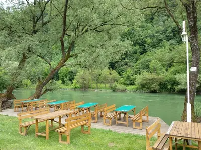a row of wooden tables and benches next to a river at Camp Vrbas in Rekavice