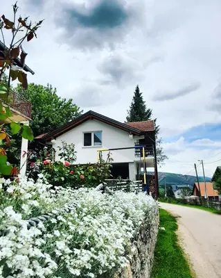 a house with white flowers in front of a stone wall at Apartment Prole in Šipovo