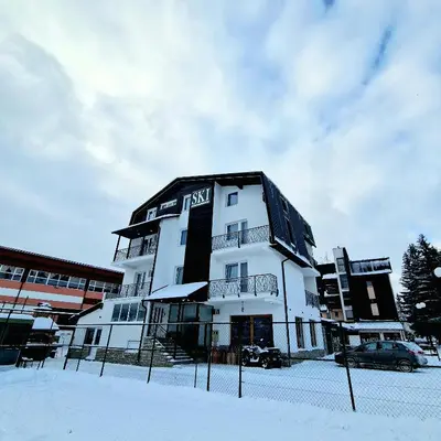 a white building with a black roof in the snow at Apartments and Rooms Ski in Vlasic