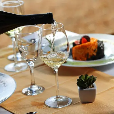 a person pouring white wine into two wine glasses on a table at Motel Restoran Gurman in Banja Luka