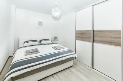 a white bedroom with a bed and a glass wall at Apartman Centar in Banja Luka