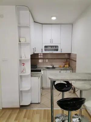 a kitchen with white cabinets and a counter and stools at Centar Apartman ENMI 111 in Banja Luka
