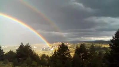 a rainbow in the sky over a field with trees at Vinara Kupres in Kupres