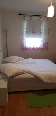 a bedroom with a bed with a window and a green rug at Brilliant Apartman in Bihać