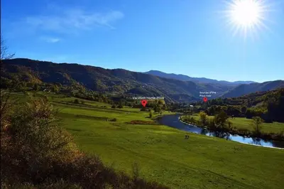 a green field with a river and mountains in the background at Vacation Home Pliva in Šipovo