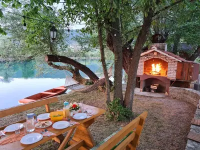 a picnic table with a fireplace next to a lake at Orhidea in Bihać