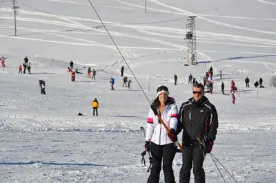 a man and woman standing in the snow next to a ski lift at Ski Rostovo - Hotel Rostovo & Ethno Village in Čardaci