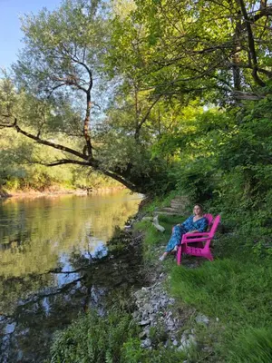 a man sitting on a pink chair next to a river at Private Riverside House on the Una River with Private Beach in Kulen Vakuf