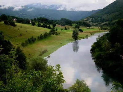 a river in a field with mountains in the background at Apartment Stanic in Šipovo
