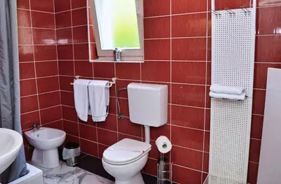 a red tiled bathroom with a toilet and a sink at Guesthouse Marivo in Jajce
