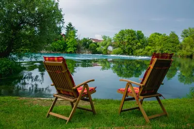 two chairs sitting on the grass near a lake at LGP Exclusive Apartment in Bihać