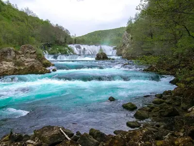 a river with blue water and rocks and a waterfall at Naid Apartmani in Kulen Vakuf