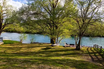 a park with trees and a bench next to the water at simply-una in Bihać