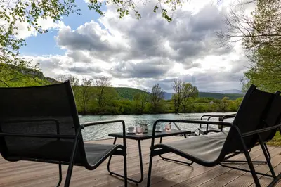 two chairs and a table on a deck next to a lake at simply-una in Bihać