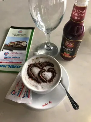 a cup of coffee on a plate next to a wine glass at Motel HEKO in Bugojno