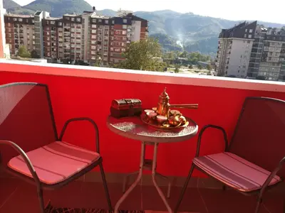 a table and two chairs on a balcony with a red wall at SWEET APT Zenica in Zenica