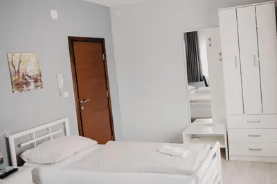 a white bedroom with a bed and a wooden door at Prenoćište Park in Modriča