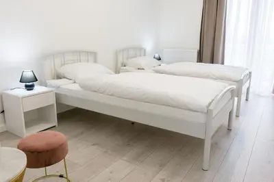 two white beds in a white bedroom with a chair at Grande Plus Apartment Dzungla in Doboj