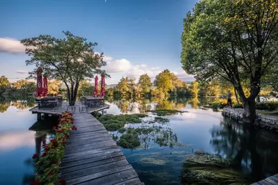 a wooden walkway over a lake with benches and trees at Apartments MLIN in Bihać