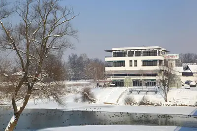 a building in the snow next to a pond at Hotel Le Pont in Prijedor