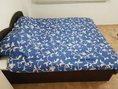 a bed with a blue blanket with white flowers on it at Apartment Centar LUX in Banja Luka