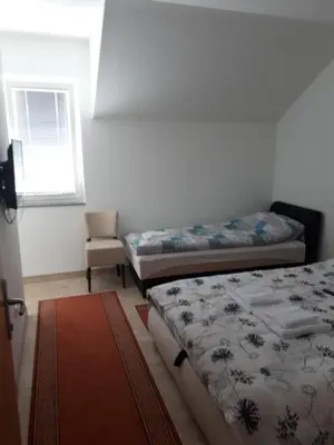 two beds in a room with a window and a chair at SOBE ROOMS GAVRILO in Banja Luka