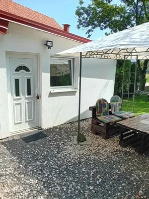 a white house with a table and chairs under an umbrella at Ravne Apartman in Visoko