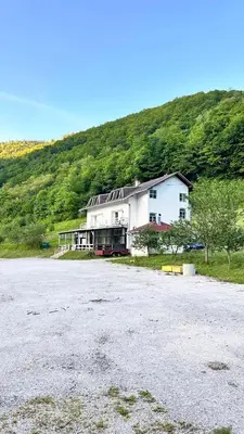 a large white building with a hill in the background at Apartman Torlakovac in Donji Vakuf
