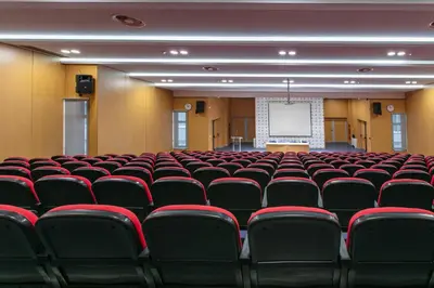 an empty lecture hall with red chairs and a whiteboard at Hotel IUT in Travnik