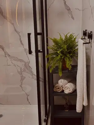 a bathroom with a shower and a shelf with towels at Apartman Deluxe Una Holiday in Bihać