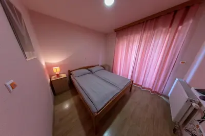 a small bedroom with a bed and a pink window at Apartments Crvena Jabuka in Ključ