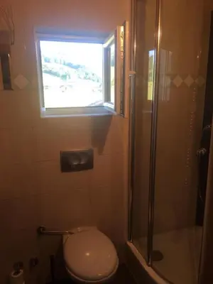 a bathroom with a toilet and a shower with a window at OMLADINSKI HOTEL ROSTOVO in Bugojno