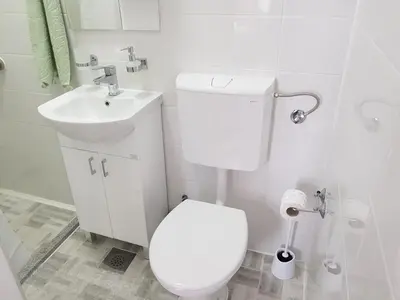 a white bathroom with a toilet and a sink at Korzo Tuzla in Tuzla
