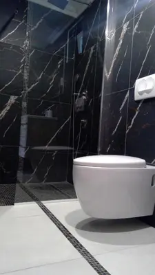 a white toilet in a bathroom with black tiles at Bungalovi Ključ in Ključ