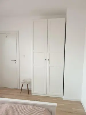 a white bedroom with white cabinets and a chair at Apartman Viktoria in Tuzla
