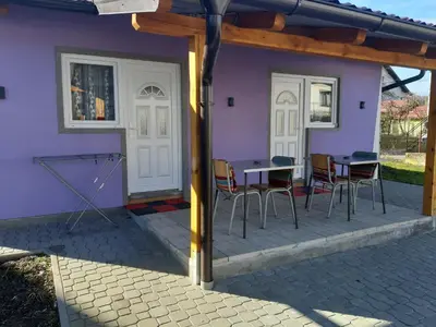 a patio with a table and chairs and a purple house at SubotićSmještaj in Kulaši
