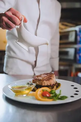 a chef is pouring sauce on a plate of food at Hotel IN in Banja Luka