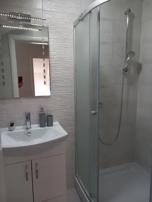 a white bathroom with a shower and a sink at Apartmani Kaić in Livno