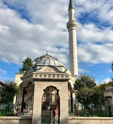 a woman standing in front of a mosque with a minaret at All White in Banja Luka
