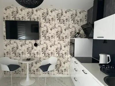 a kitchen with white chairs and a tv on a wall at Apartman CITY CENTER 2 in Prijedor