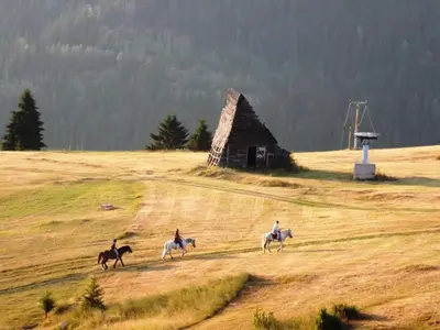 three people riding horses in a field with a barn at Apartman SARA Babanovac Vlašić in Travnik